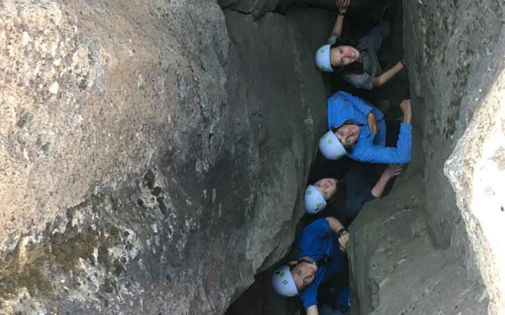 a group of students looks up and smile as they stand in a crevice between two rock walls